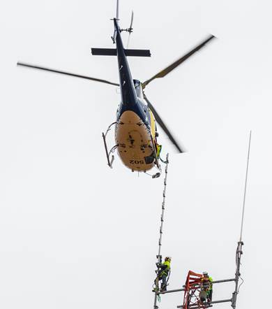 A helicopter assisting with installation of antennas on a SAGRN tower.